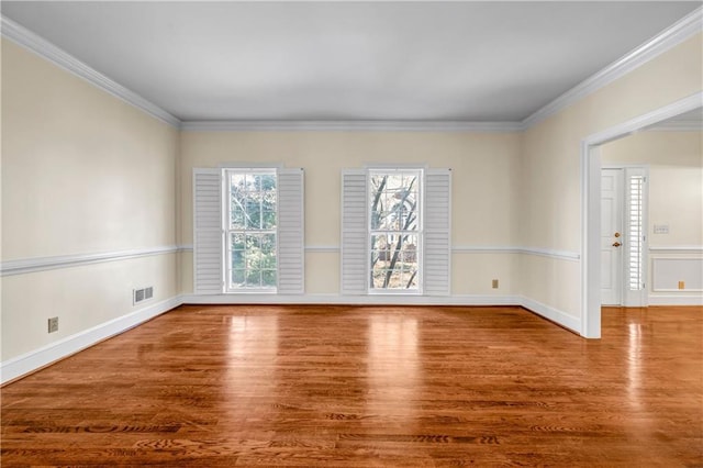 empty room featuring visible vents, ornamental molding, baseboards, and wood finished floors