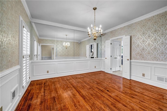 unfurnished dining area with visible vents, wood finished floors, wainscoting, wallpapered walls, and a chandelier