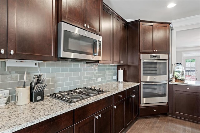 kitchen featuring light stone counters, decorative backsplash, dark brown cabinetry, and appliances with stainless steel finishes