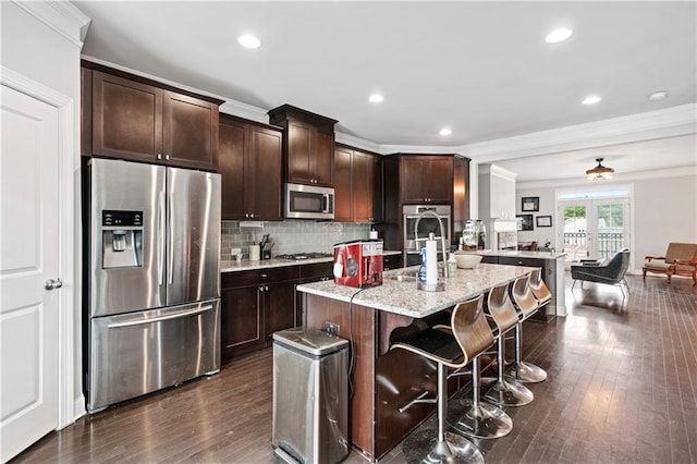 kitchen featuring dark brown cabinets, stainless steel appliances, light stone countertops, an island with sink, and a kitchen bar