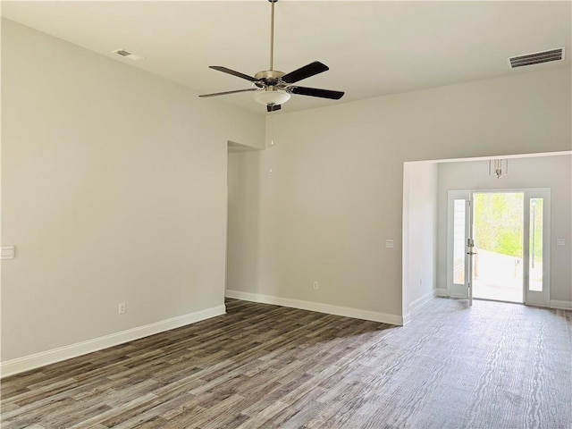 empty room with baseboards, a ceiling fan, wood finished floors, and visible vents