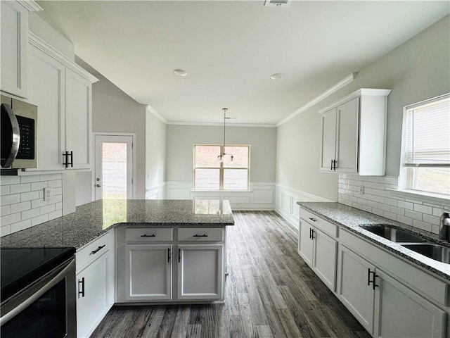 kitchen featuring a peninsula, stainless steel microwave, a healthy amount of sunlight, and ornamental molding