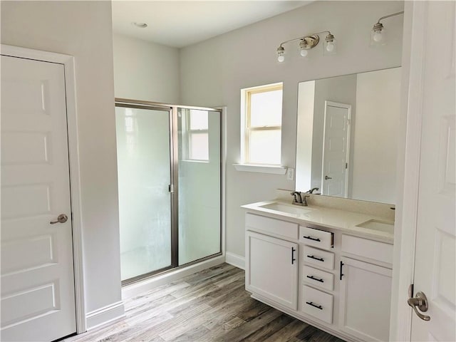 bathroom with double vanity, a sink, wood finished floors, and a shower stall