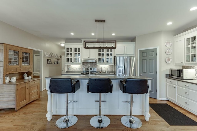 kitchen featuring stainless steel appliances, decorative light fixtures, a center island with sink, and white cabinets