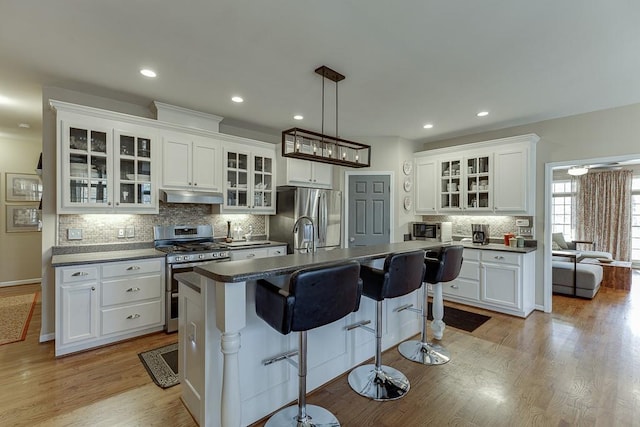 kitchen featuring a breakfast bar, white cabinetry, decorative light fixtures, a center island with sink, and appliances with stainless steel finishes