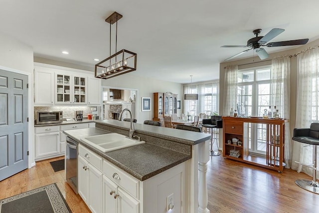 kitchen featuring sink, white cabinets, hanging light fixtures, stainless steel appliances, and a center island with sink