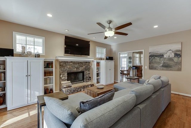 living room with a stone fireplace, light hardwood / wood-style flooring, and ceiling fan