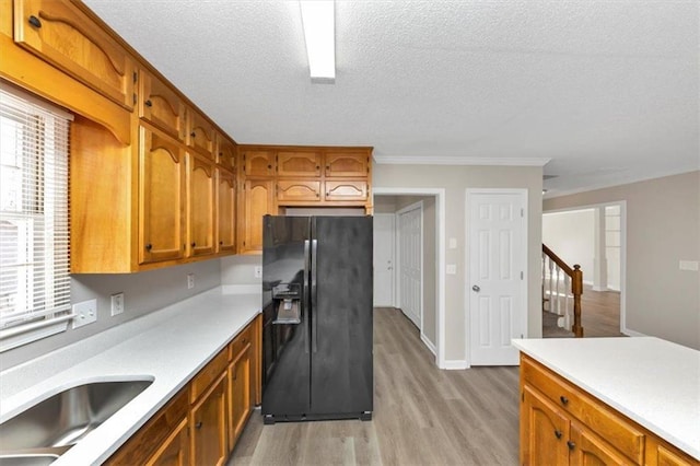 kitchen with sink, ornamental molding, light hardwood / wood-style floors, a textured ceiling, and black refrigerator with ice dispenser