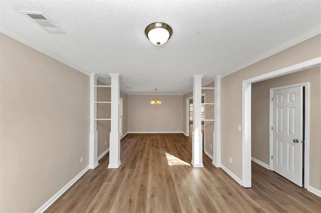 unfurnished living room featuring crown molding, wood-type flooring, a textured ceiling, a chandelier, and ornate columns