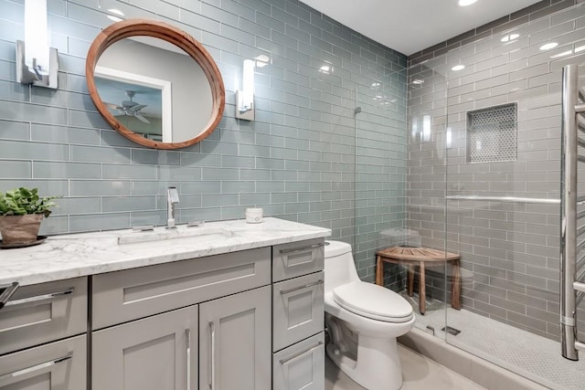 bathroom with tile walls, vanity, an enclosed shower, ceiling fan, and toilet