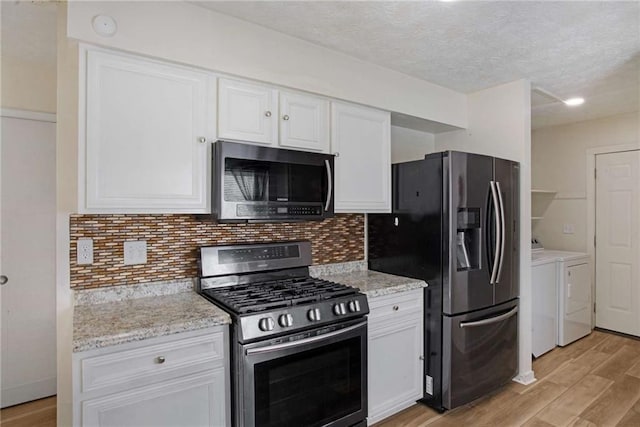 kitchen with appliances with stainless steel finishes, backsplash, washing machine and clothes dryer, white cabinets, and light hardwood / wood-style floors