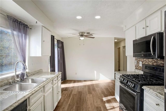 kitchen with light wood-type flooring, ceiling fan, sink, white cabinets, and stainless steel gas stove