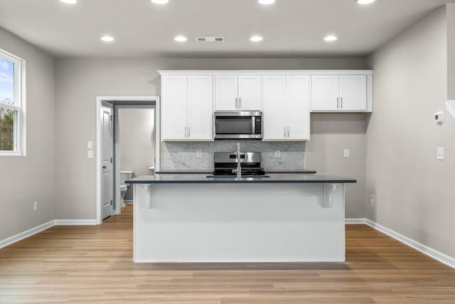 kitchen featuring white cabinetry, appliances with stainless steel finishes, a kitchen island with sink, and light hardwood / wood-style flooring