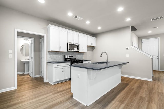 kitchen with sink, appliances with stainless steel finishes, white cabinetry, wood-type flooring, and an island with sink