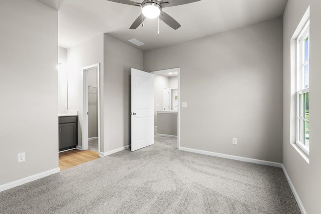 unfurnished bedroom featuring connected bathroom, a walk in closet, ceiling fan, light carpet, and a closet