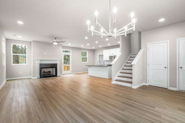 unfurnished living room with sink, a premium fireplace, ceiling fan, and light wood-type flooring