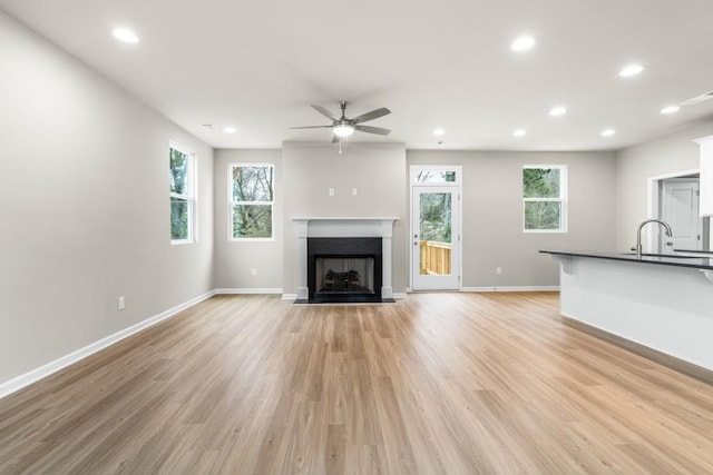 unfurnished living room featuring sink, ceiling fan, and light wood-type flooring