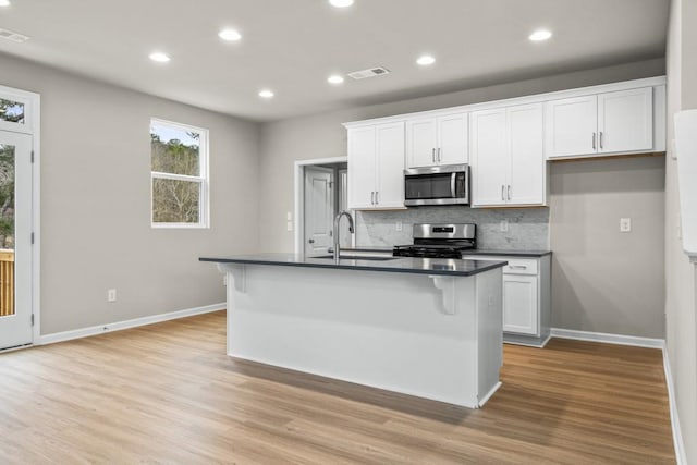 kitchen featuring stainless steel appliances, white cabinetry, and a kitchen island with sink