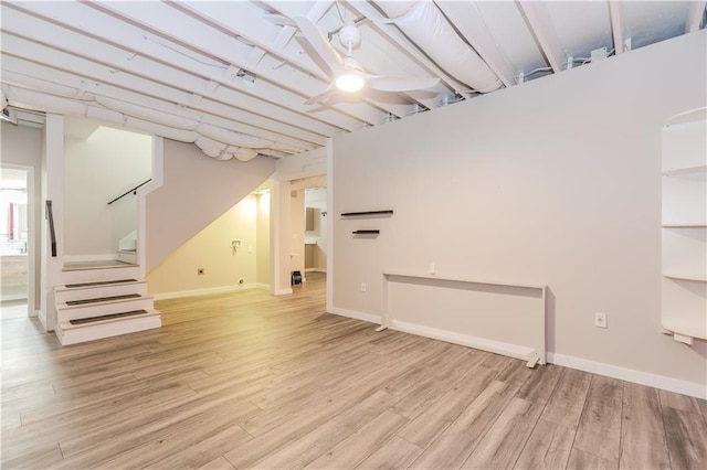 below grade area with light wood finished floors, stairway, a ceiling fan, and baseboards