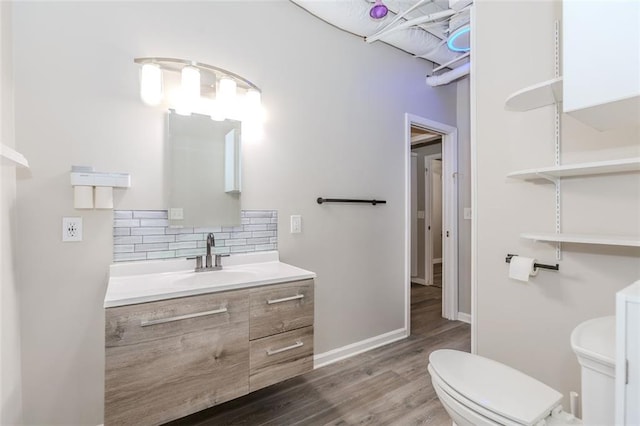 bathroom featuring backsplash, toilet, vanity, wood finished floors, and baseboards