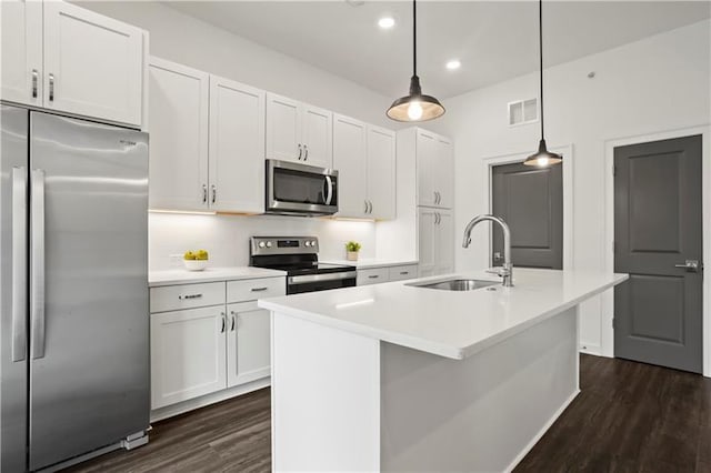 kitchen with appliances with stainless steel finishes, sink, white cabinets, hanging light fixtures, and an island with sink