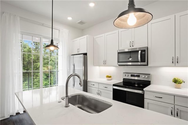 kitchen with tasteful backsplash, stainless steel appliances, sink, decorative light fixtures, and white cabinets