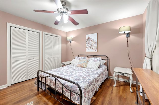 bedroom featuring baseboards, ceiling fan, two closets, and wood finished floors