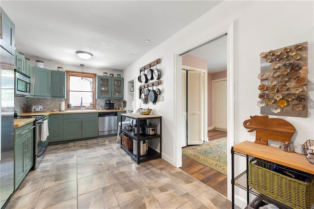 kitchen with a sink, stainless steel appliances, backsplash, light countertops, and green cabinets
