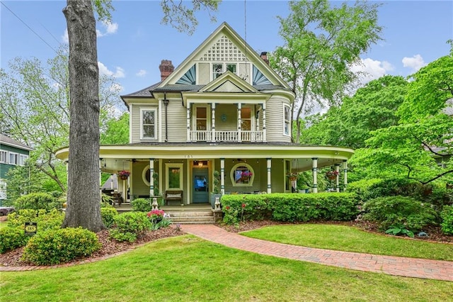 victorian home featuring a porch, a balcony, a front yard, and a chimney