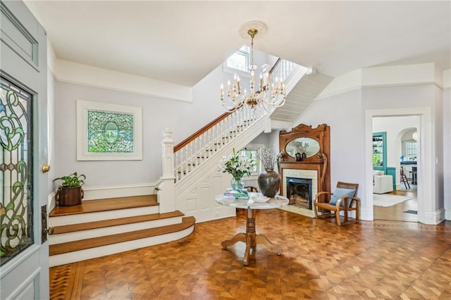 foyer with stairs, a notable chandelier, a wealth of natural light, and a fireplace