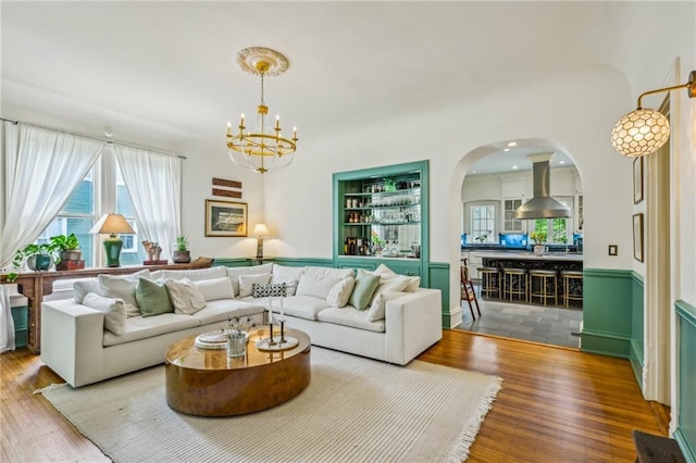 living area featuring arched walkways, built in features, wood finished floors, and a notable chandelier
