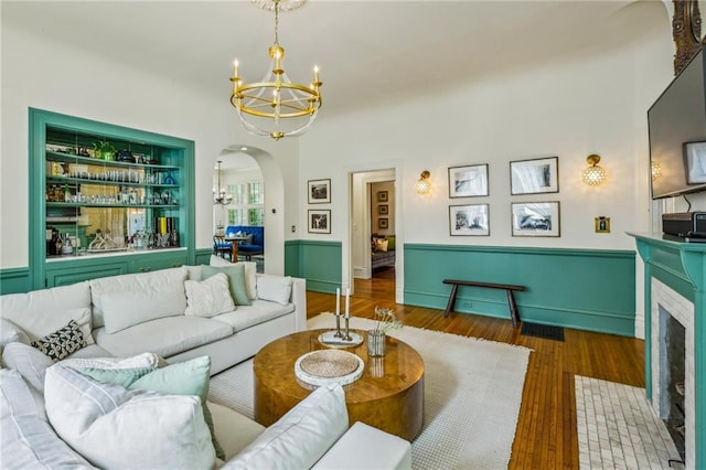 living area featuring visible vents, a fireplace with flush hearth, wood finished floors, arched walkways, and a notable chandelier