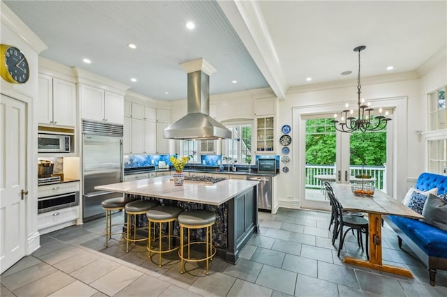 kitchen with island range hood, appliances with stainless steel finishes, a chandelier, a breakfast bar, and white cabinetry