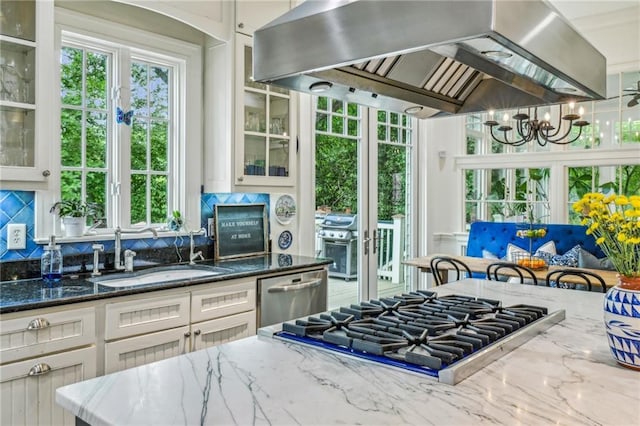 kitchen featuring stone countertops, wall chimney range hood, a sink, a notable chandelier, and stainless steel appliances