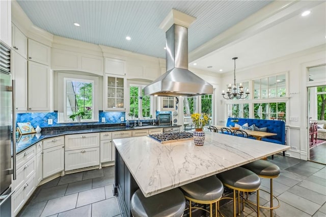 kitchen featuring a kitchen island, a kitchen bar, dark stone counters, tasteful backsplash, and island exhaust hood