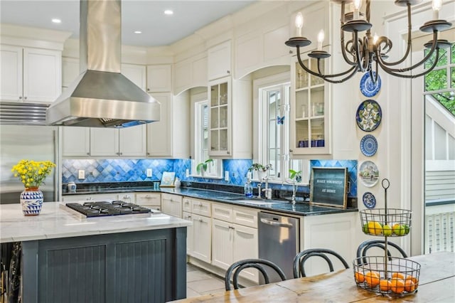 kitchen featuring island exhaust hood, a sink, dark stone countertops, an inviting chandelier, and stainless steel appliances