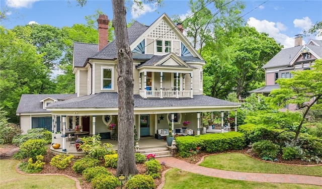 view of front of house with a porch, a chimney, a balcony, and roof with shingles
