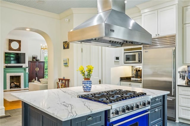 kitchen with exhaust hood, light stone counters, built in appliances, arched walkways, and white cabinetry