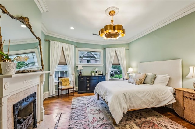 bedroom with visible vents, crown molding, wood-type flooring, an inviting chandelier, and a premium fireplace