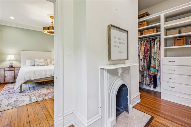 bedroom with a closet, ornamental molding, wood finished floors, and a fireplace
