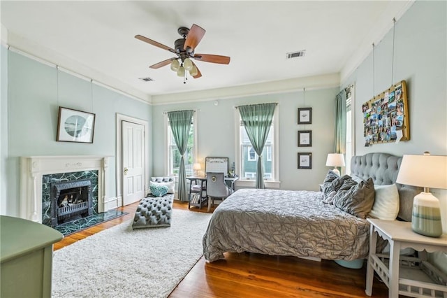 bedroom featuring a ceiling fan, visible vents, wood finished floors, and a high end fireplace