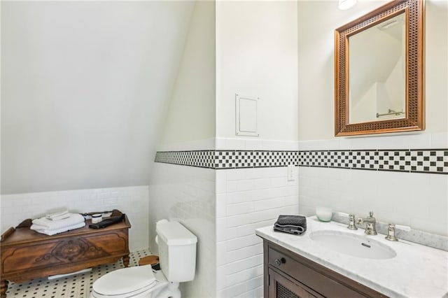 bathroom with tile walls, a wainscoted wall, vanity, and toilet
