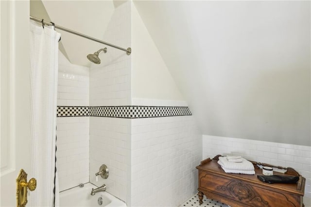 bathroom featuring tile walls, shower / bath combo, lofted ceiling, and a wainscoted wall