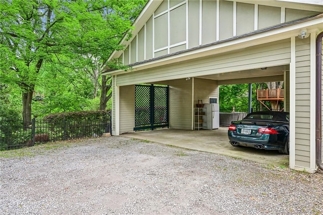 view of parking with fence, driveway, and a carport