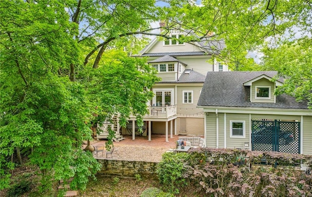rear view of property with stairway, a patio, a wooden deck, and a shingled roof