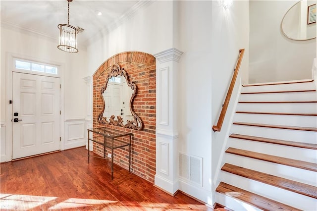 entryway with a notable chandelier, wood-type flooring, and crown molding