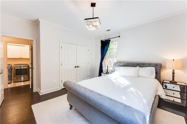 bedroom with washer and clothes dryer, a closet, ornamental molding, dark hardwood / wood-style flooring, and a chandelier