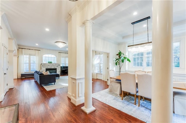 interior space featuring decorative columns, a stone fireplace, dark wood-type flooring, and crown molding