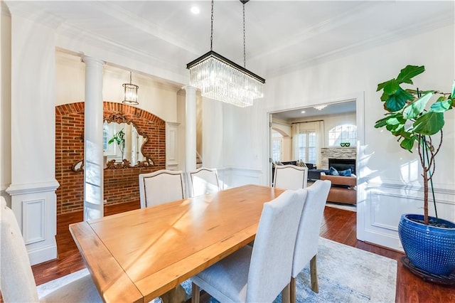 dining space featuring ornate columns, brick wall, a chandelier, dark hardwood / wood-style floors, and a stone fireplace