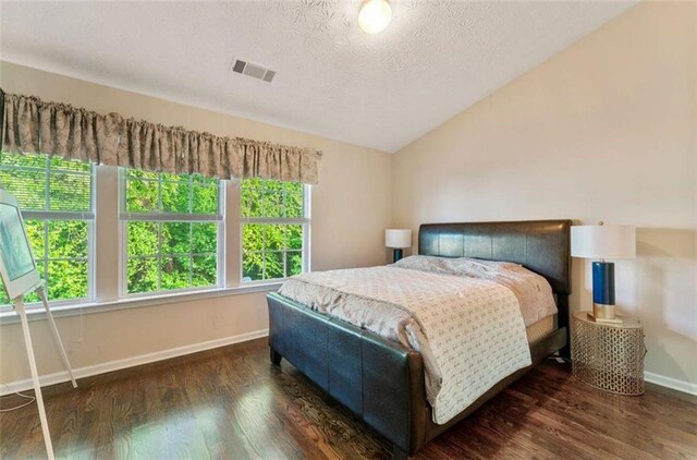 bedroom with a textured ceiling, lofted ceiling, and dark wood-type flooring